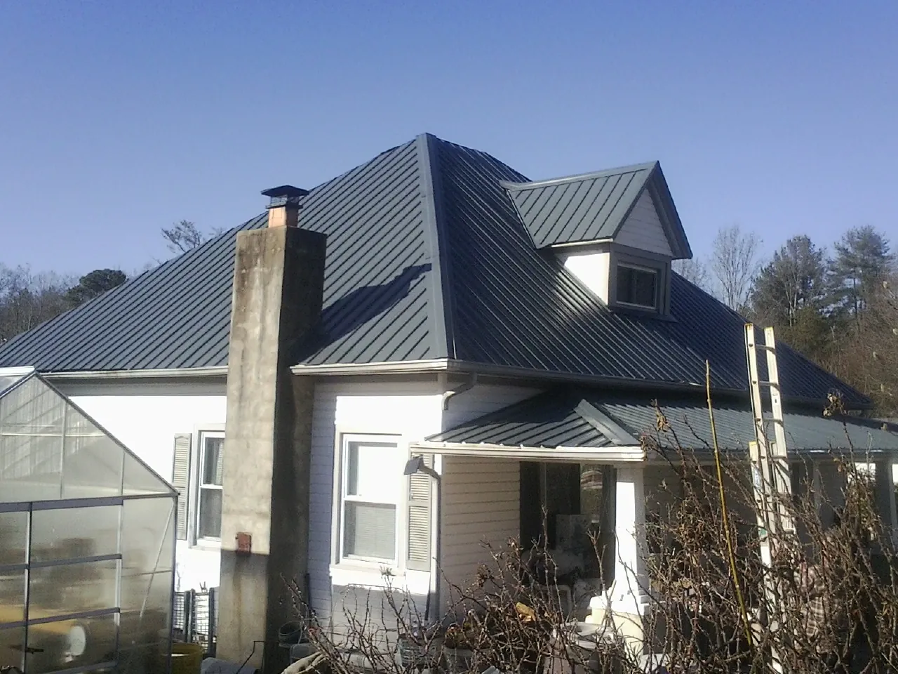 Dark blue standing seam metal roof on a white farmhouse with dormer — Slate & Tile Roof Repair by Roofing Brothers in Arkansas City