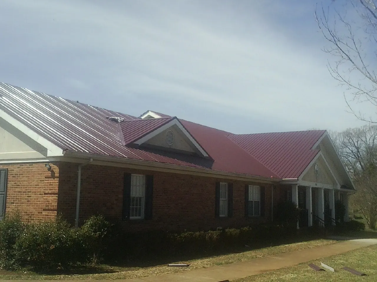 Red metal roof with gabled entries on a long brick building, from a Hail Damage Roof Repair job in Arkansas City