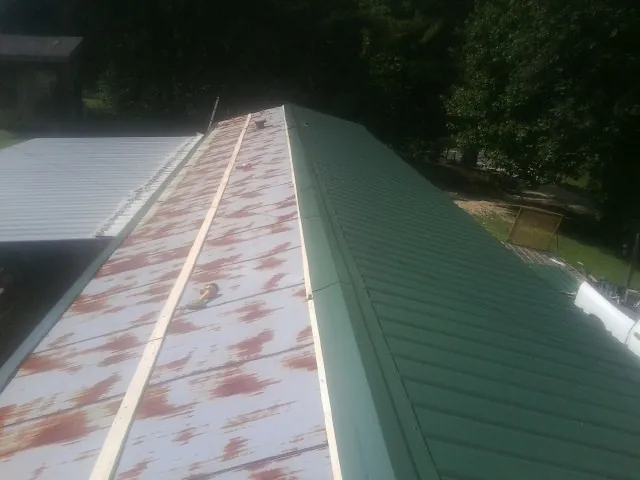 Old rusted panels beside newly installed green metal roofing — Wind Damage Roof Repair by Roofing Brothers in Arkansas City