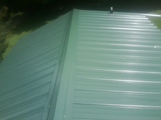New green metal panels meeting at the ridge of a roof — Flat Roof Repair work by our crew in Arkansas City