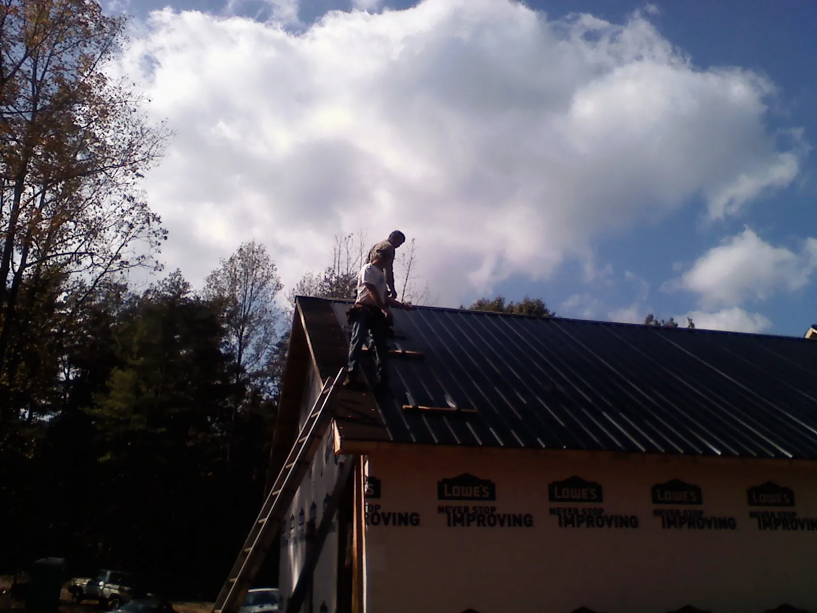Roofer fastening dark metal panels high against a cloudy sky, from a Roof Inspection job in Arkansas City
