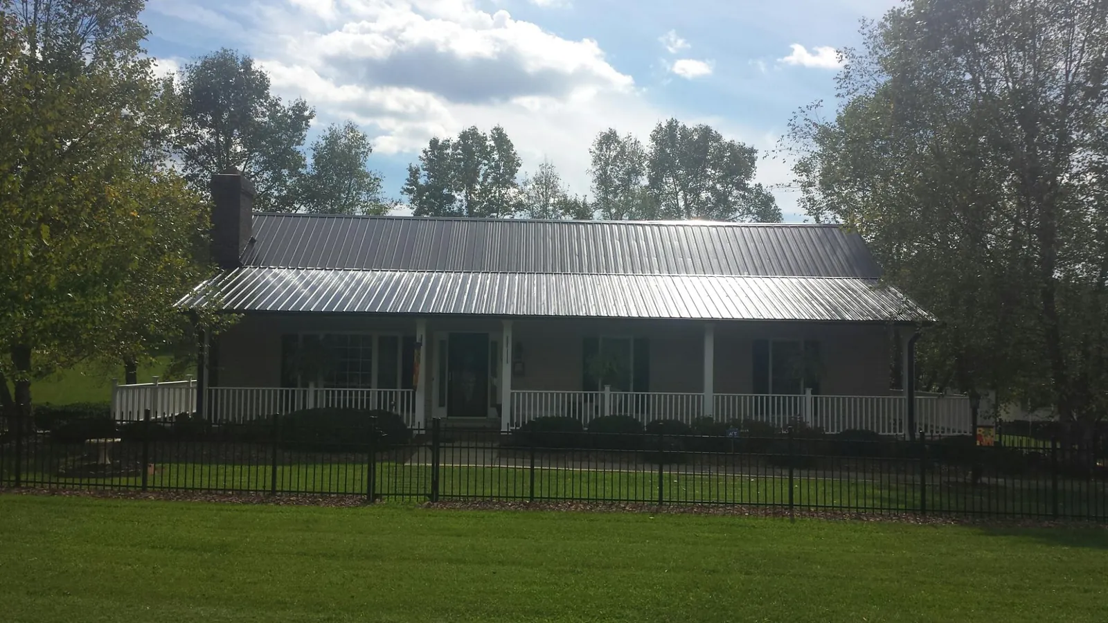 Gray metal roof on a brick ranch with a full width front porch — Gutter Guard Installation work by our crew in Arkansas City