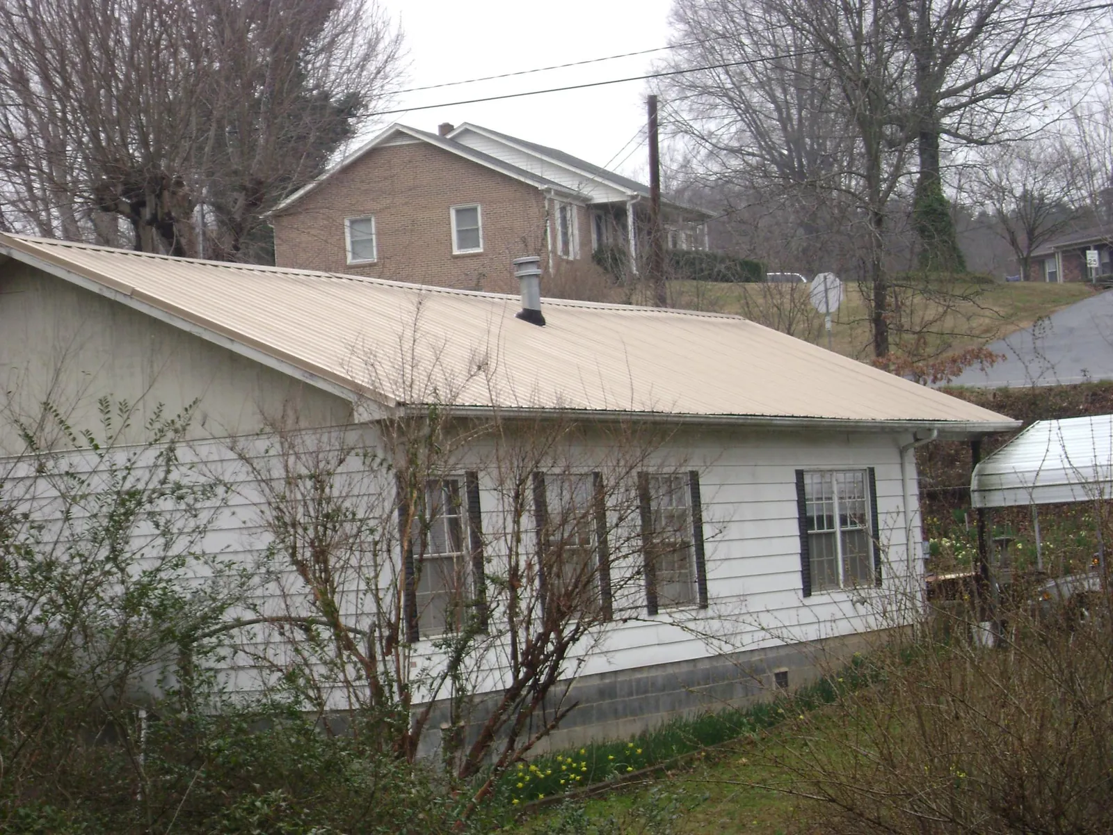 Tan metal roof on a white sided house set into a hillside — Commercial Roofing by Roofing Brothers in Arkansas City